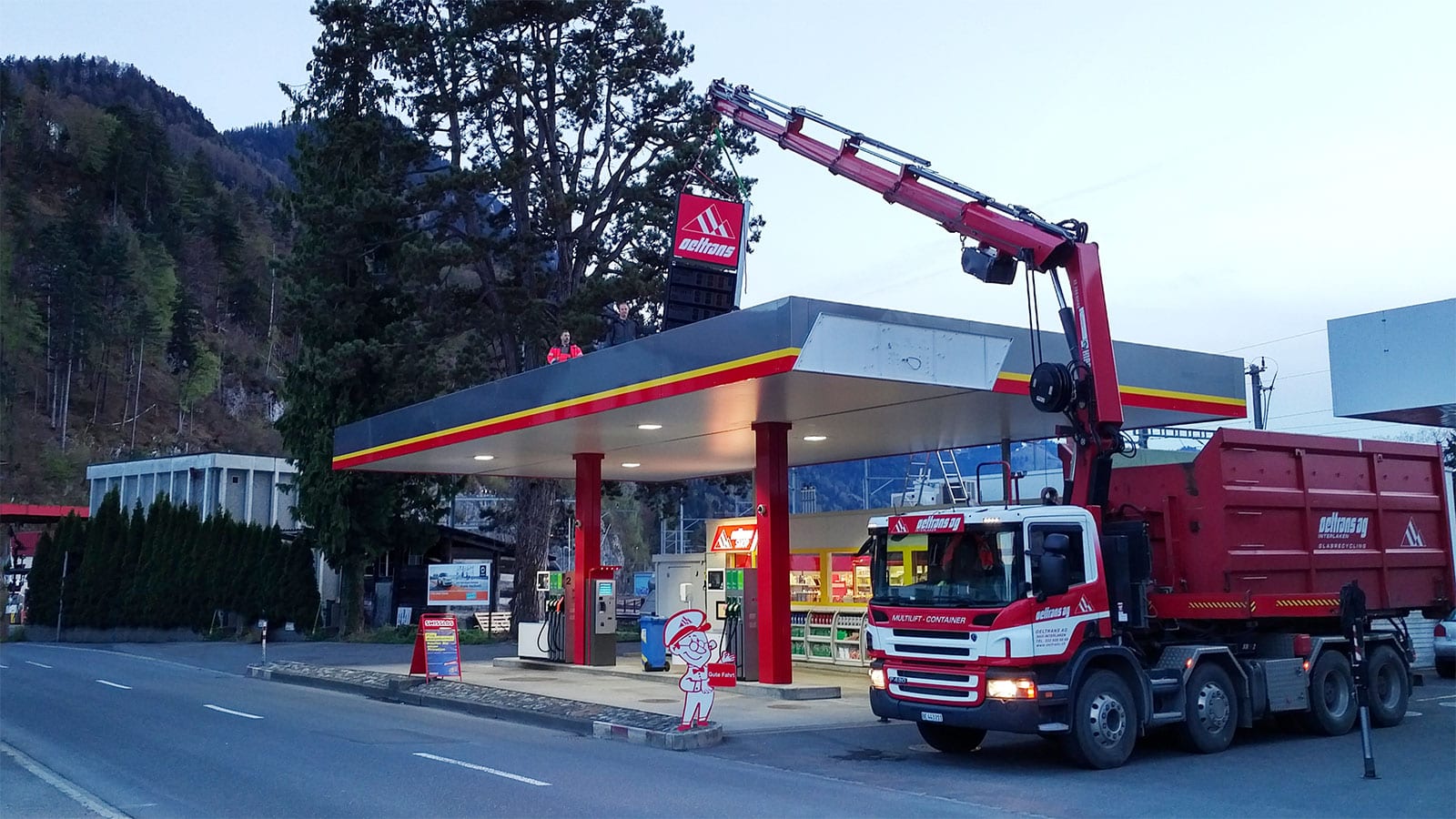 oeltrans Kranfahrzeug montiert in der Abenddämmerung ein Schild auf ein Tankstellendach
